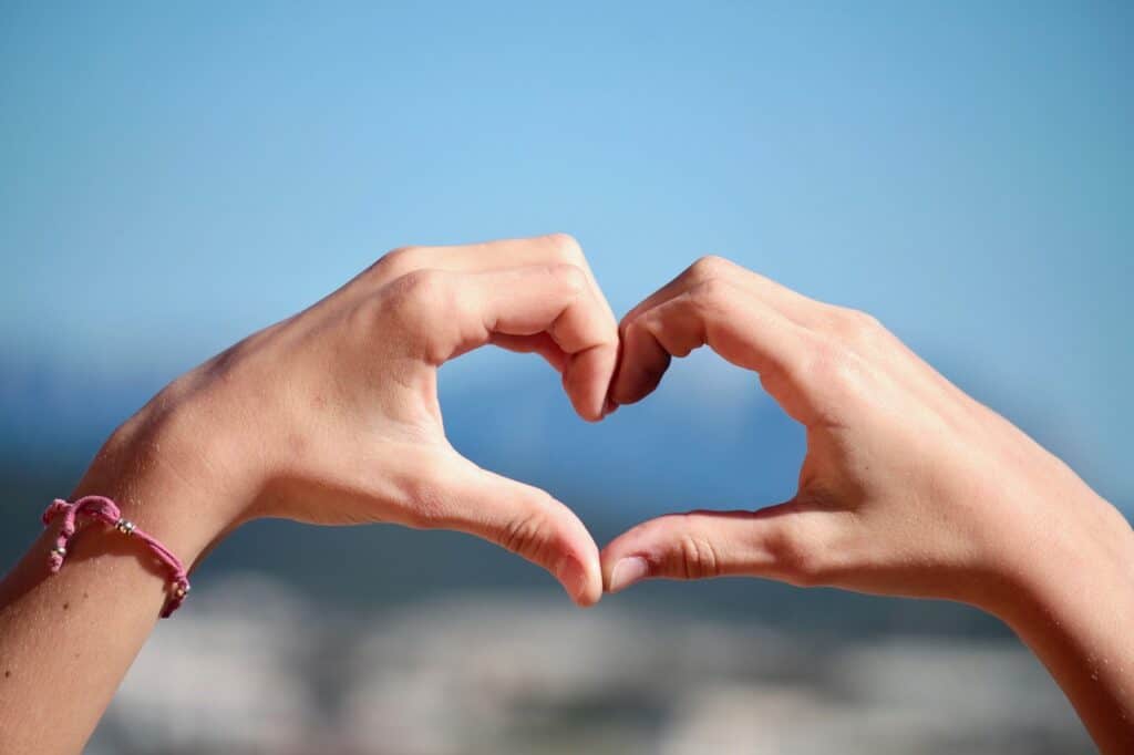 Symbol of love, two hands forming a heart, blue background.