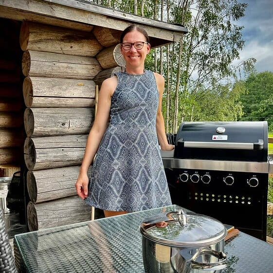Näyttävä nainen grillaa ulkona Suomen Kotteria -mökillä. Perinteinen ulkogrilli, rauhallinen luonnon ympäristö.
