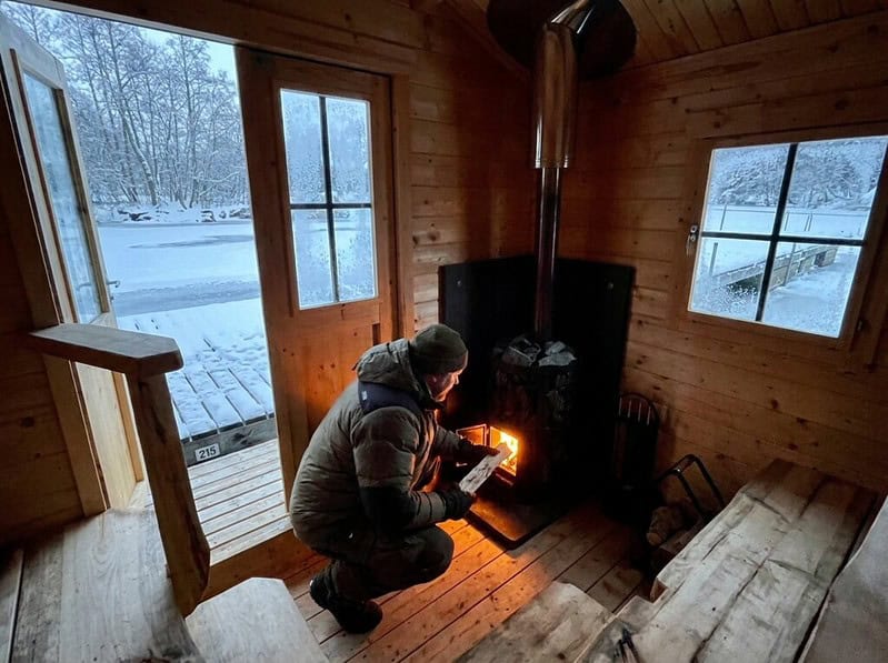 Lauttasauna käytettävissä myös talvella. Mies lisää puita kiukaan pesään